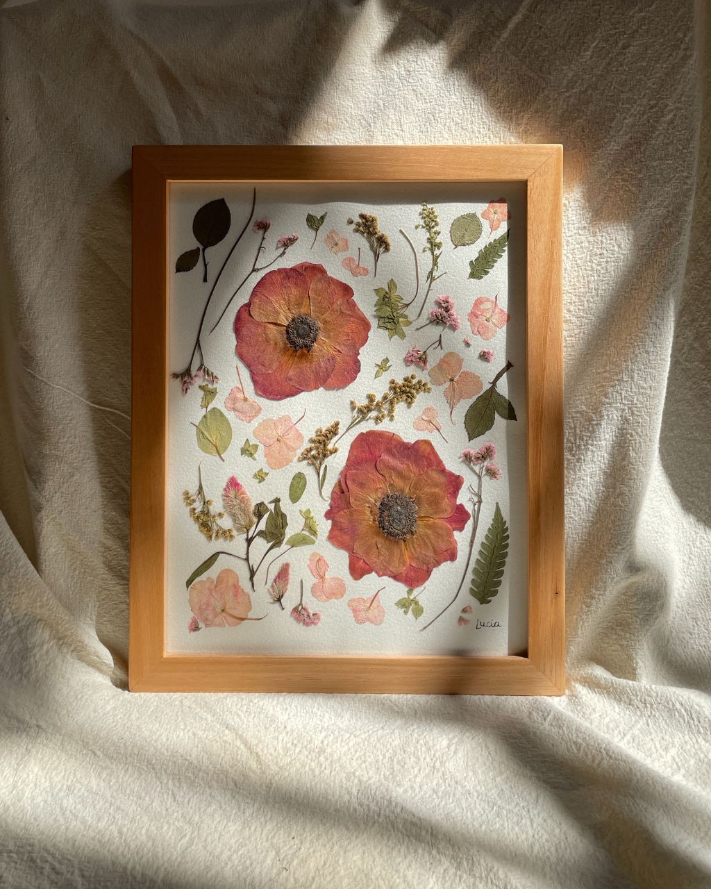 Cuadro de flores en tonos rojizos, prensadas artesanalmente y enmarcadas en marco de madera nautral y vidrio.